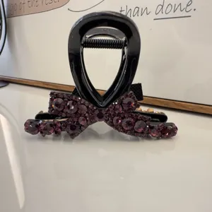 Vue détaillée d'une élégante pince à cheveux noire décorée de strass en cristal violet.