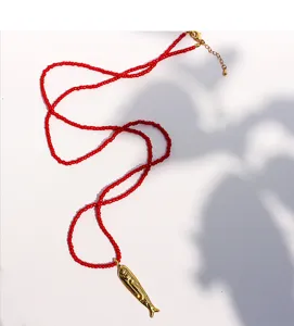 Golden fish pendant red bead necklace detail, showcasing artisan craftsmanship and vacation style.