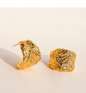 Gedetailleerde close-up van gestructureerde gouden C-vormige oorbellen met gesmolten lavadesign.