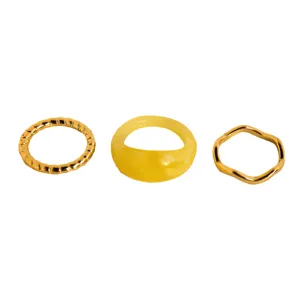 Ensemble de bagues empilables plaquées or avec métal torsadé, résine jaune et anneaux ondulés.