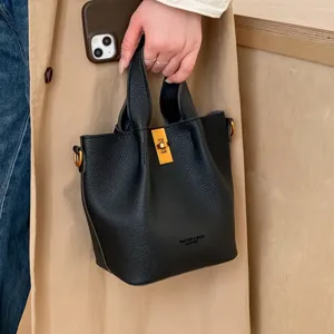 Retro minimalist black leather bucket bag with metal lock, chic top-handle bag for women spring.