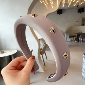 Detailed view of a wide padded headband in grayish purple, featuring metallic gold cross studs.