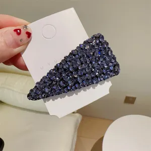 Gros plan detail d'une pince a cheveux triangulaire en strass bleu fonce scintillant.