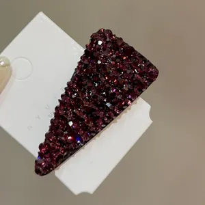 Gros plan détaillé d'une pince à cheveux triangulaire en strass violet foncé sur carte.