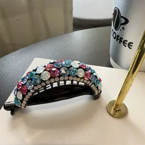 Gros plan d'une pince a cheveux courbée ornée de strass colorés sur une base noire élégante.