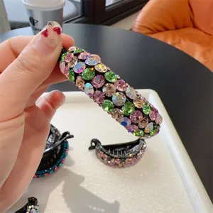Vue détaillée de pince à cheveux banane en strass, pierres colorées sur support vertical noir.