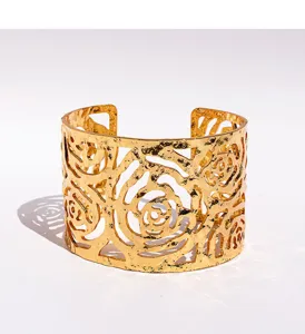 Close-up detail of the wide gold cuff bracelet featuring hollow rose floral design and texture.