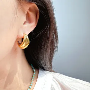 Close-up detail of geometric wave metal hoop earrings worn on ear, stylish modern jewelry.