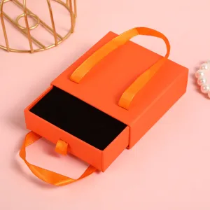 Catola portagioie a cassetto arancione con manico in nastro, ideale per anelli e bracciali.