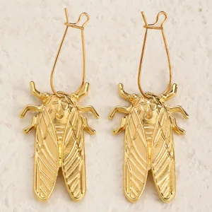 Dettaglio di orecchini pendenti cicala oro, gioiello design insetto creativo alla moda.