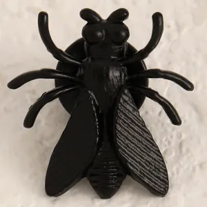 Primo piano dettaglio del gioiello di modo nero a forma di insetto con ali e texture realistiche.