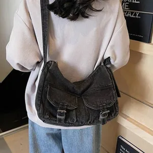 Close-up detail of casual dark grey denim crossbody bag with dual front pockets and metal buckles.