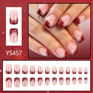 Detailweergave van korte vierkante neppe nagels met rode glitter en kerst sneeuwvlok patronen.