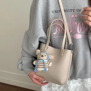Stylish beige PU leather bucket bag with cute bear pendant, top handles and shoulder strap.