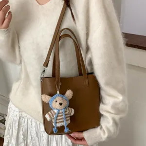 Chic brown leather bucket bag with cute knit bear pendant, versatile shoulder crossbody bag.