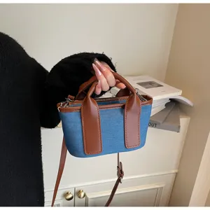 Primo piano dettagliato di una piccola borsa in denim blu con manici in pelle marrone e tracolla.
