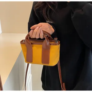 Primo piano dei dettagli della mini borsa in tela bicolore con manici in pelle marrone.