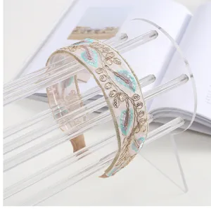Close-up detail of embroidered wide headband with gold thread and sequins on clear acrylic stand.