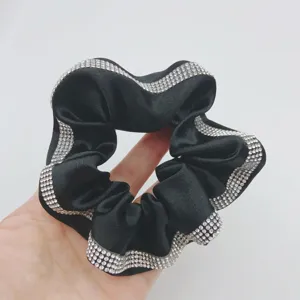 Detail view of a black satin hair scrunchie featuring shiny rhinestone edge design.