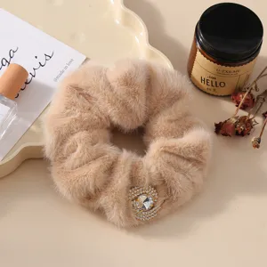 Close-up detail of fluffy plush hair scrunchie with sparkling rhinestone ornament in warm tone.