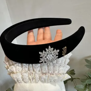 Close-up of black velvet headband with crystal snowflake and gold logo detail.