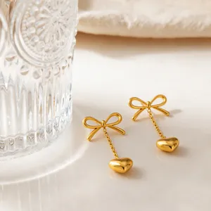Detailed close-up of minimalist gold-tone stainless steel bowknot heart drop earrings.