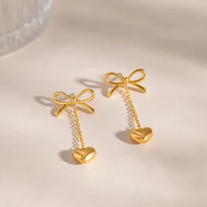 Detailed shot of gold-plated stainless steel bow and heart dangling chain stud earrings.