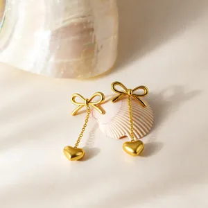 Gold bow heart dangle earrings detail view showing polished stainless steel finish and fine chain.