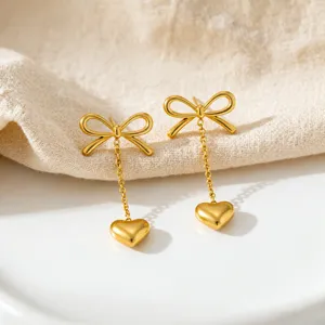 Close-up of gold bow and heart dangle earrings featuring delicate chains and elegant design.