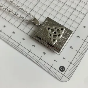 Detailed close-up shot of the silver book locket pendant necklace on a grid measuring mat.
