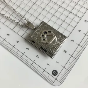 Detailed close-up of a silver book-shaped locket necklace with a cute paw print design.