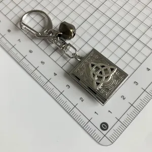 Portachiavi a libro gotico vintage in argento con simbolo triquetra e campanello piccolo.