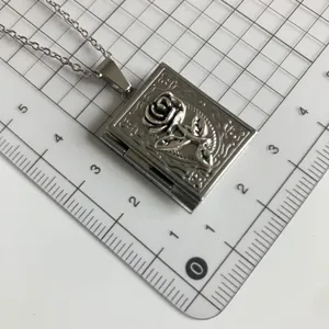 Silver vintage book locket necklace with rose relief pendant on grid background detail.