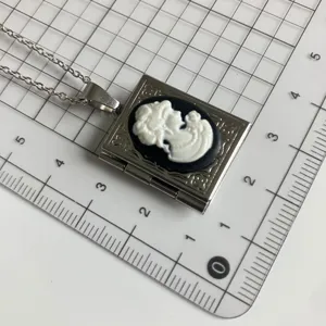 Close-up detail of vintage book locket necklace with black white cameo pendant on grid background.