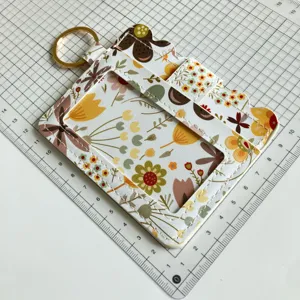 Detailed closeup of a floral print ID card holder with golden keyring on a grid craft mat.