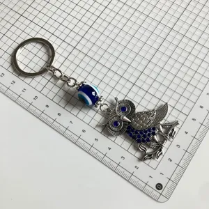 Detailed view of retro owl metal keychain with evil eye glass bead on grid measuring mat.
