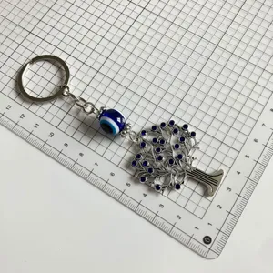 Details of evil eye key ring with tree pendant and blue rhinestones on grid background.