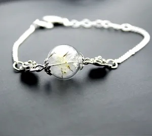 Primo piano di un bracciale argento con sfera di vetro trasparente contenente veri semi di soffione.