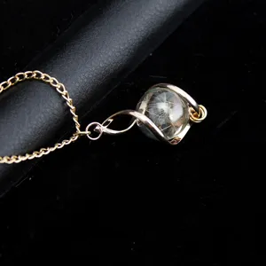 Close-up of a delicate gold chain necklace featuring a glass pendant with natural dandelion seeds.