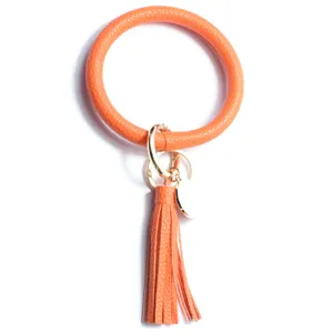 Gros plan sur le porte-clés bracelet rond en cuir orange avec pompon et anneau métallique.
