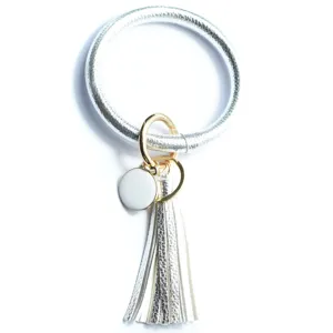Close-up van de zilveren PU lederen cirkel sleutelhanger met kwastje en wit rond bedel detail.