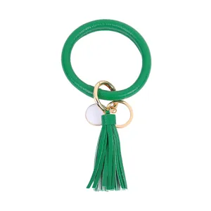 Detailopname van groene PU lederen cirkel sleutelhanger met kwastje en gouden ring.
