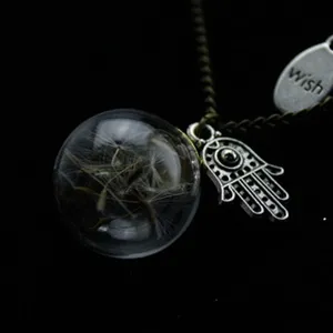 Detailed close-up of a glass globe pendant necklace with real dandelion seeds and hamsa charm.