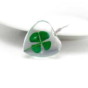 Close-up detail shot of a clear heart-shaped resin pendant featuring a real green four-leaf clover.