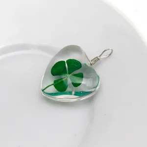 Heart-shaped crystal resin pendant with real four-leaf clover specimen and silver wire.