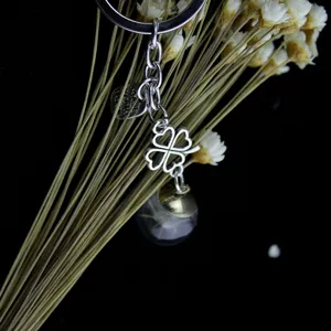 Detailaufnahme des Metall-Schlüsselanhängers mit Kleeblatt-Charm und Glaskugel mit Pusteblume.