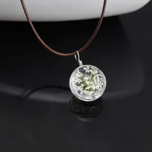 Close-up of a clear glass ball pendant necklace featuring delicate dried white flowers inside.