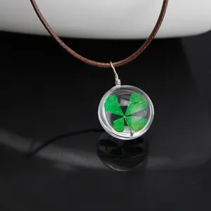 Close-up view of a clear glass ball necklace featuring a real green four leaf clover.