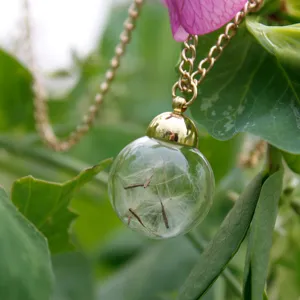 Detailed view of glass globe dandelion seed pendant necklace with gold chain and botanical charm.