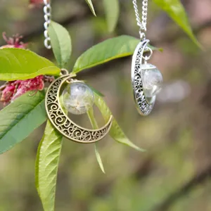 Detail view of natural dandelion seeds inside a glass globe crescent moon necklace.